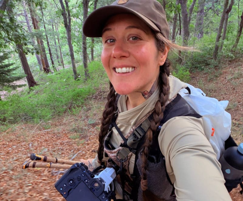 Outdoor photographer wearing the Hyperlite Mountain Gear Aero 28 backpack and carrying a camera on a forested hiking trail.