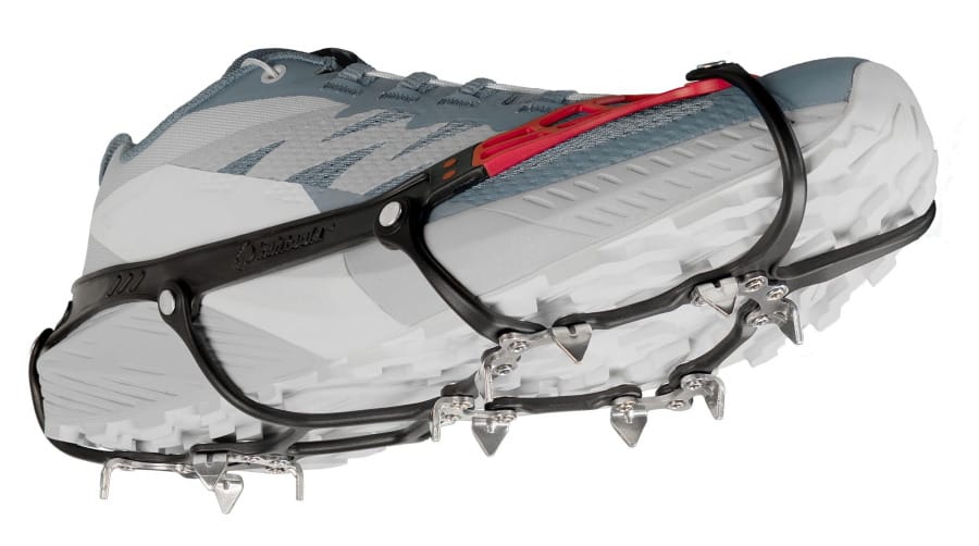 Kahtoola MICROspikes Ghost traction device fitted over a gray and white trail running shoe, showing the black harness, red upper section, and metal traction spikes.