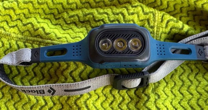 Close-up of the Black Diamond Deploy 325 headlamp resting on a green fleece, showing the compact body, triple-LED light design, and lightweight elastic strap.