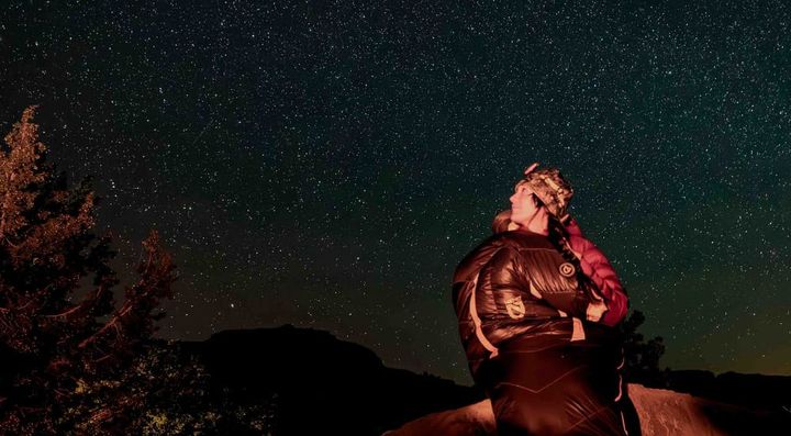 a winter backpacker sits outside in her nemo equipment sonic -20° down ultralight sleeping bag under a sea of stars
