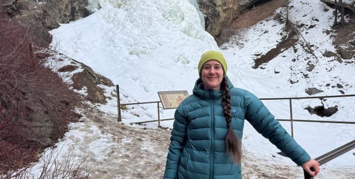 a hiker wears the Eos Down Jacket By Feathered Friends at a frozen waterfall and she stays warm