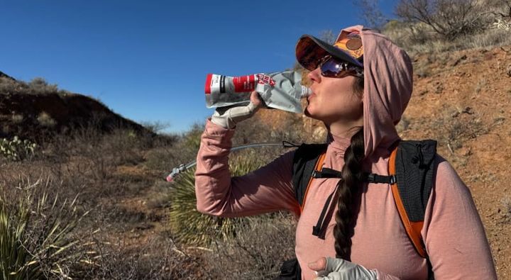 a woman drinks a Recpak One Complete Meal while out on a big backpacking adventure in the southwest