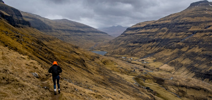 Hiker wearing a rain jacket walking through a moody, windswept valley surrounded by mountains.
