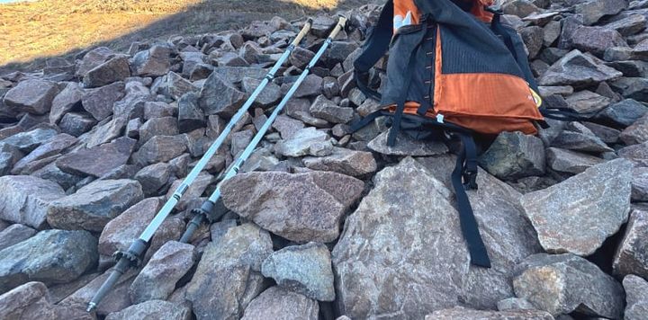  LEKI Cressida FX Carbon AS trekking poles folded next to an orange and black backpack on a rocky mountain slope.