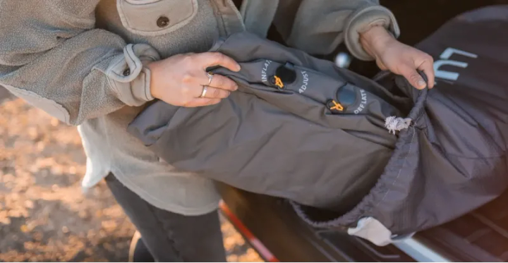  Camper packing up a Luno inflatable mattress and deflation valves into its storage bag after a night on the road.