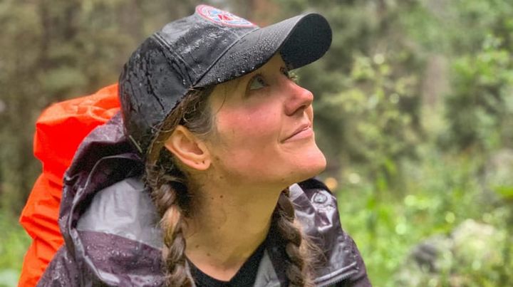 Smiling woman in braids and rain gear hiking in the forest during a rainy day.