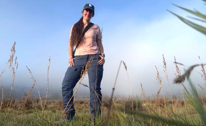 Woman wearing the Fjallraven Keb Trousers in a grassy field with fog in the background, showcasing the improved fit for Summer 2025.