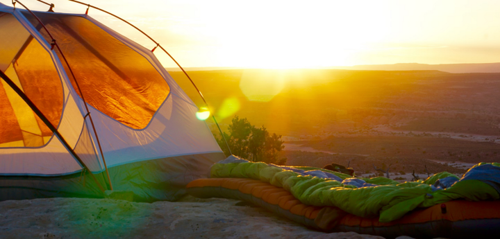  Sunset over desert canyon with a tent and sleeping bag in the foreground, showing affordable camping gear setup.