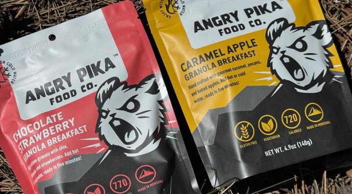  Angry Pika Food Co. Chocolate Strawberry and Caramel Apple granola breakfast pouches on pine needles outdoors.