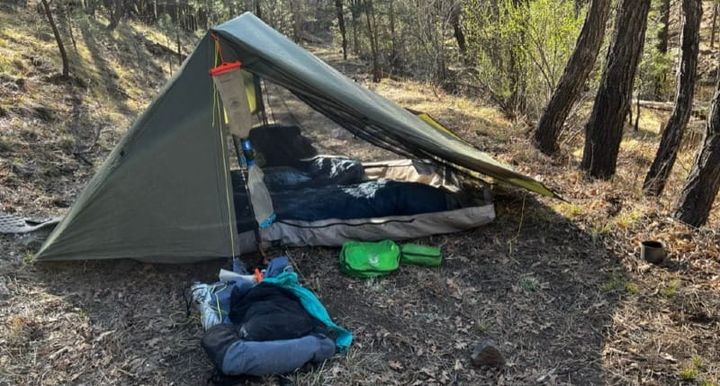 Six Moon Designs Haven Tent set up in a forested campsite, showing sleeping bags and water filtration gear under the tarp.