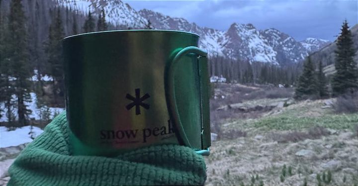  Snow Peak titanium mug held in gloved hand with snowy mountain landscape in the San Juan Mountains in the background.