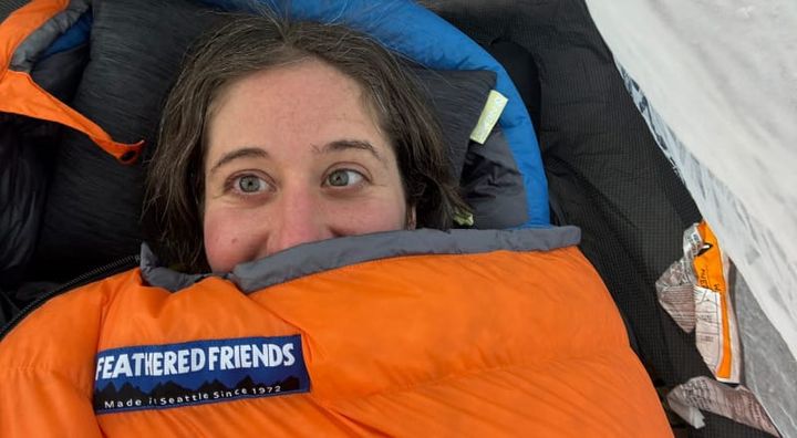 Smiling hiker bundled in a Feathered Friends Egret sleeping bag inside a tent.