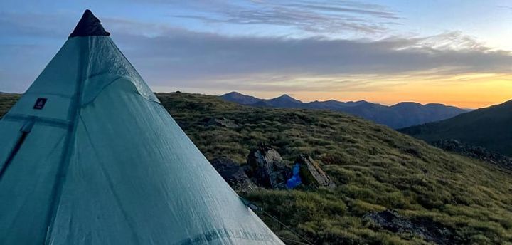  Hyperlite Mountain Gear UltaMid shelter set up in an alpine meadow at sunset with mountain views in the distance, showcasing ultralight backcountry camping.