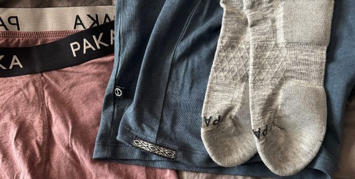 Flatlay image showing the PAKA Essential Tee, boxer briefs, mid-rise briefs, and Trail Ankle Socks on a bed