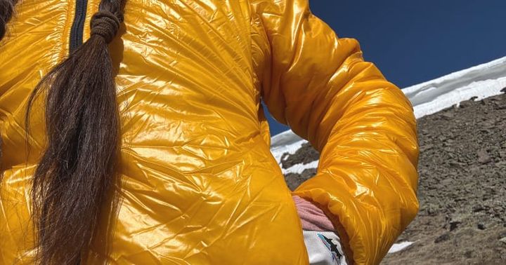 Close-up of a hiker wearing a bright yellow Enlightened Equipment puffy jacket in the alpine, promoting the 2025 Enlightened Equipment November Sale offering 20% off sitewide.