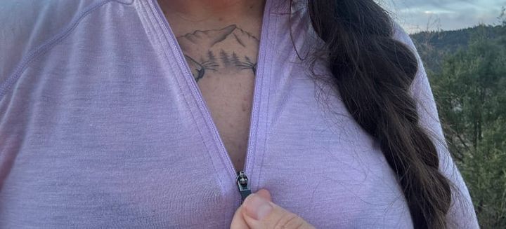 Deirdre Denali Rosenberg zipping up the lilac Ibex Woolies Pro Tech Half Zip merino base layer outdoors, showing collar and fit detail in natural light.