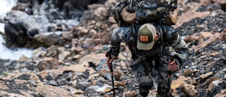 Hunter wearing KUIU performance jacket and pack in mountain terrain during the 2025 Black Friday Sale, promoting up to 50% off ultralight hunting and backcountry gear.