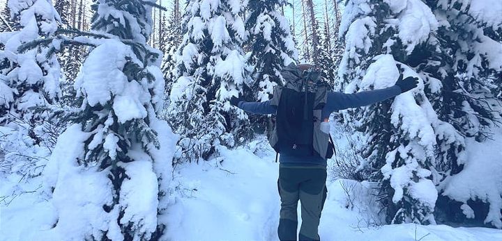 Backpacker wearing the Outdoor Vitals Shadowlight Carbon 60 in a snow-covered forest with arms outstretched, showing pack fit and winter performance.