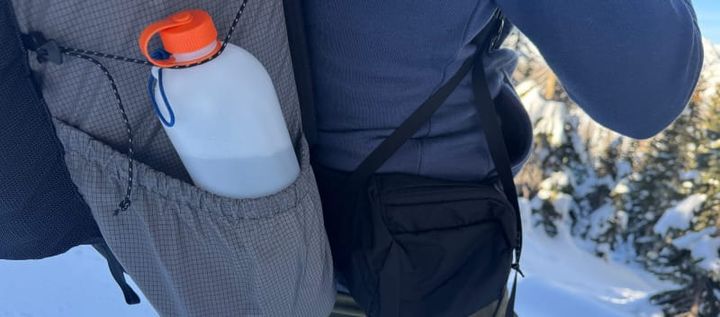 Close-up of the CNOC ThruBottle stored in a backpack side pocket during a snowy hike.