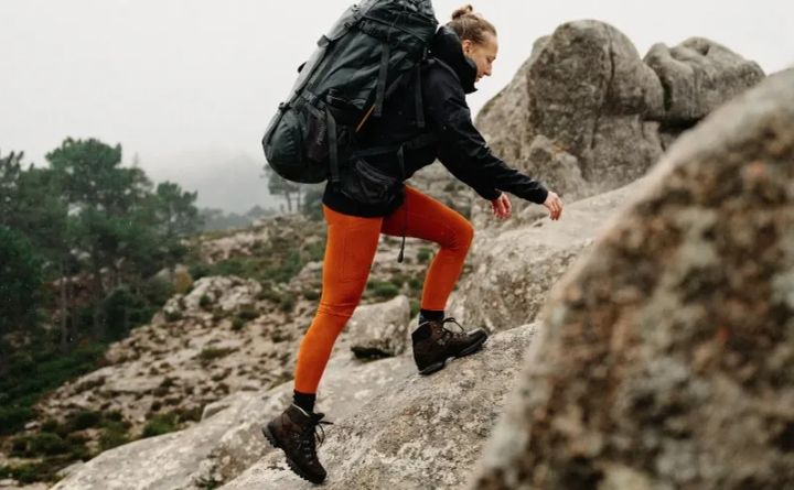 Female hiker wearing Fjallraven Abisko Trekking Tights while climbing over rocky terrain with a large backpack in misty mountain conditions.