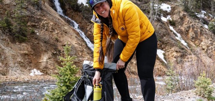 hiker wearing branwyn essential compressive leggings made of wool in black she is near a river using her backpack