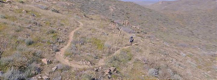 Backpacker hiking on an exposed desert trail while testing the best sun hoodies for hiking and backpacking in 2026.