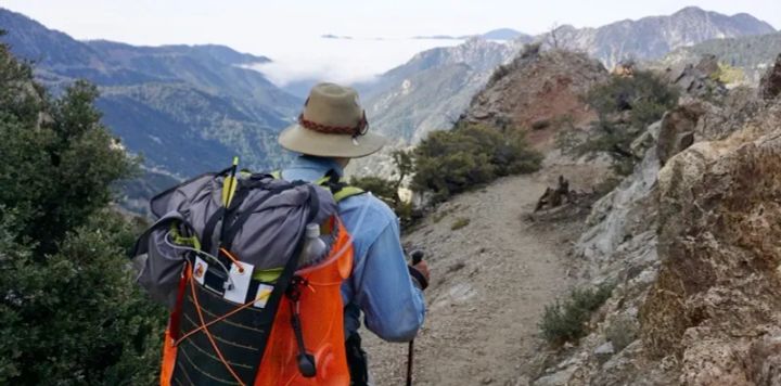 Hiker wearing a Chicken Tramper Ultralight Gear backpack on a narrow mountain trail, showcasing an ultralight pack built for long-distance backpacking. and small gear for organization.