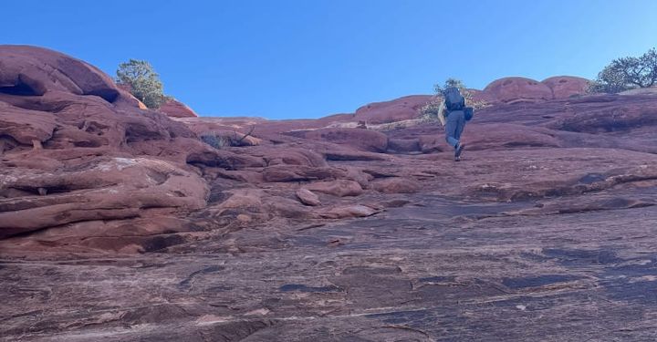 Hiker ascending steep red rock slickrock terrain wearing Salewa Puez 2 Mid Powertex hiking boots under clear blue desert skies