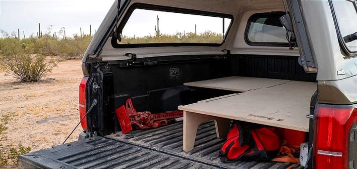 BamBeds solo truck camping platform in Toyota Tacoma with open tailgate showing partial bed setup and extra cargo space.