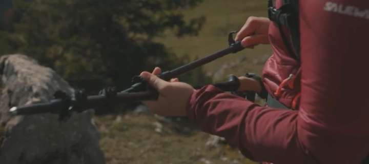 Hiker unfolding LEKI Black Series FX Carbon trekking pole outdoors in mountain terrain, showing quick folding design and lightweight carbon construction.