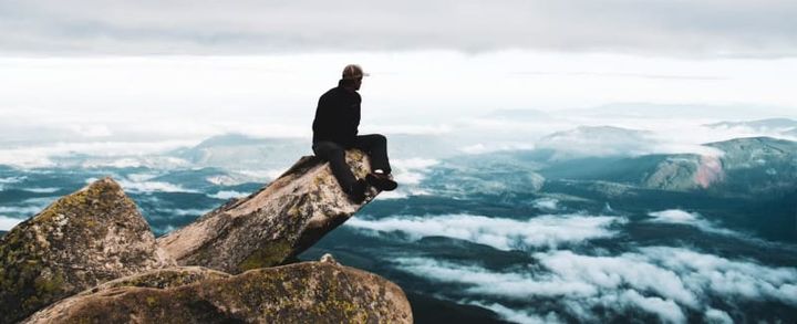 Hiker wearing a hiking jacket on a rocky mountain summit above the clouds, featured in the Best Hiking Jackets of 2026 guide.