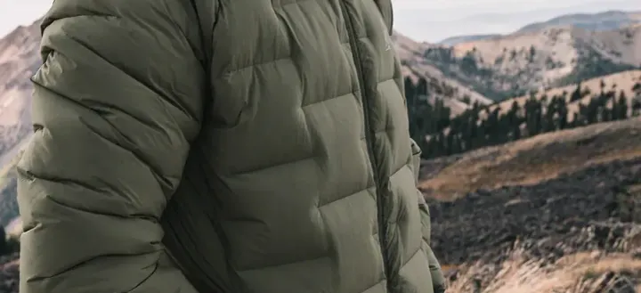 Hiker wearing an insulated green down jacket in cold, high-elevation mountain terrain.