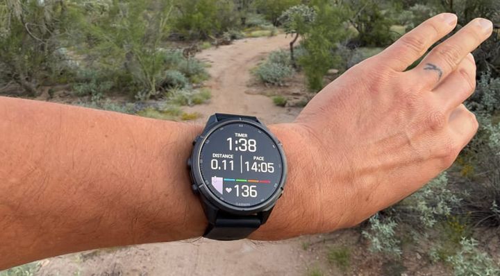 Garmin fēnix 9 Pro inReach GPS smartwatch worn during a hike in Arizona's Sonoran Desert, displaying distance, pace, elapsed time, and heart rate against a desert trail backdrop.