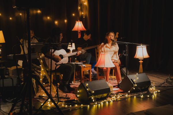 The Macarons Project performing an intimate show for their album release, featuring acoustic guitars, soft lighting, and warm