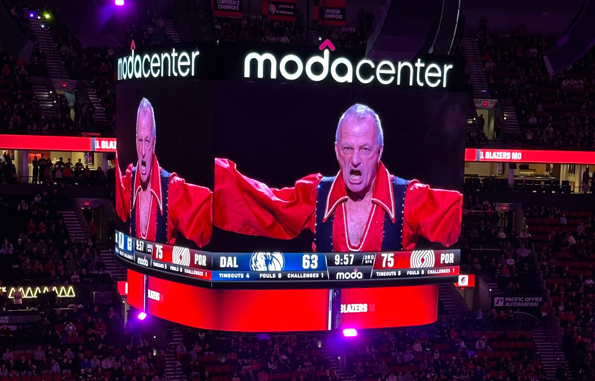 The Amazing Sladek shouting on the jumbotron at the Moda Center. He's wearing a red shirt open 1/4 way down his chest.