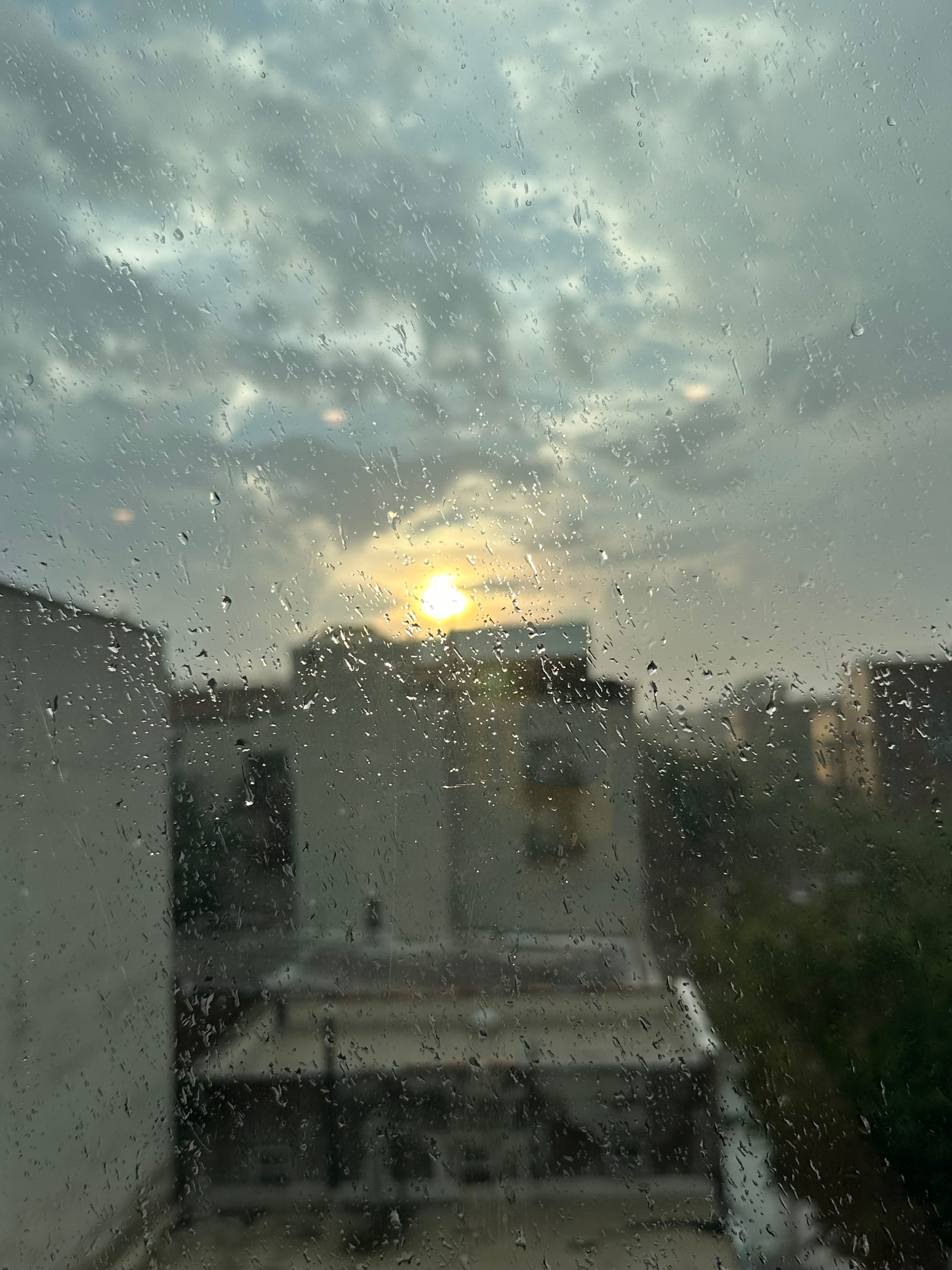 a blurry sunset behind the brooklyn skyline through a rain-spattered window