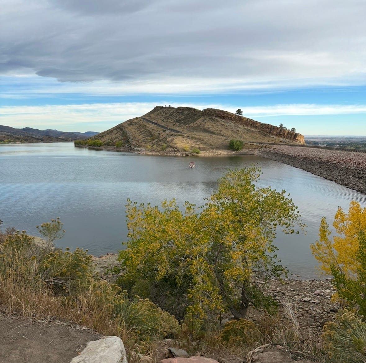 Horsetooth Reservoir, with a little bota in the water, and a hill with a trail up it in the distance.