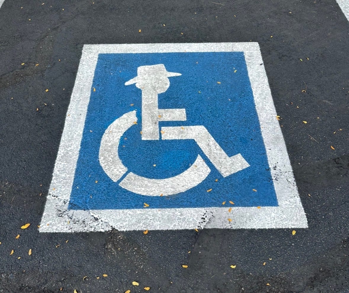 Classic handicap spot marking but the person in the wheelchair is wearing a bold hat.