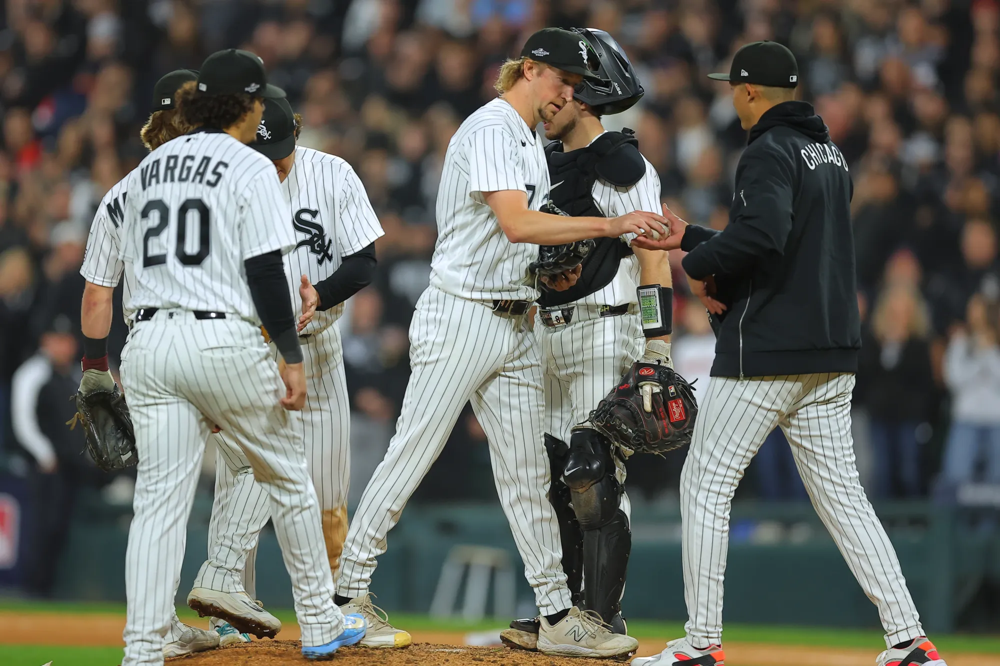 White Sox pitcher on the mound handing the ball over to a coach/manager with other players gathered around.