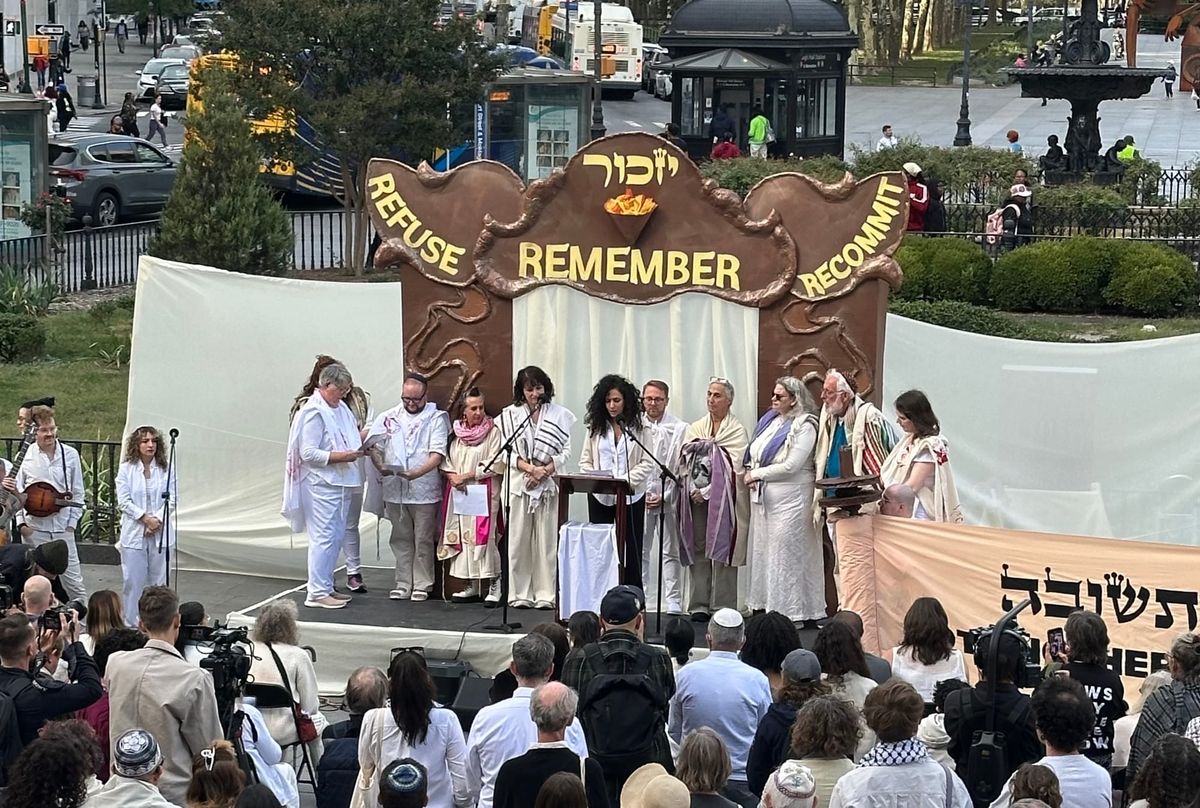 Hala Alyan speaking at a Yizkor service in Brooklyn surrounded by rabbis with some onlookers.