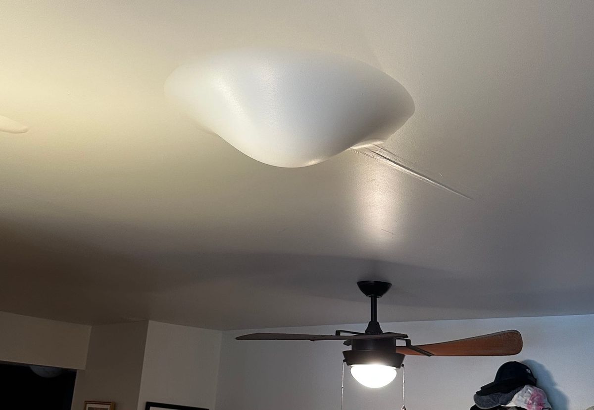 Big bulging water damage on my ceiling with a ceiling fan in the background for scale. Also some hats, not important.