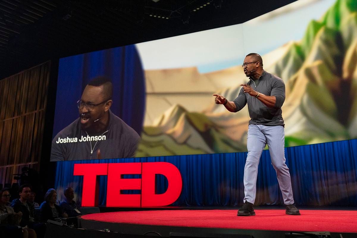 Joshua Johnson, Creator/Moderator of The Resolution, on stage at TED2026: All of Us in Vancouver. Joking that "Idiots are everywhere", he presents his concept of objectivity over neutrality.