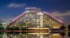 Night photo of a hotel on the edge of a river. The lights of the hotel are reflected in the river.