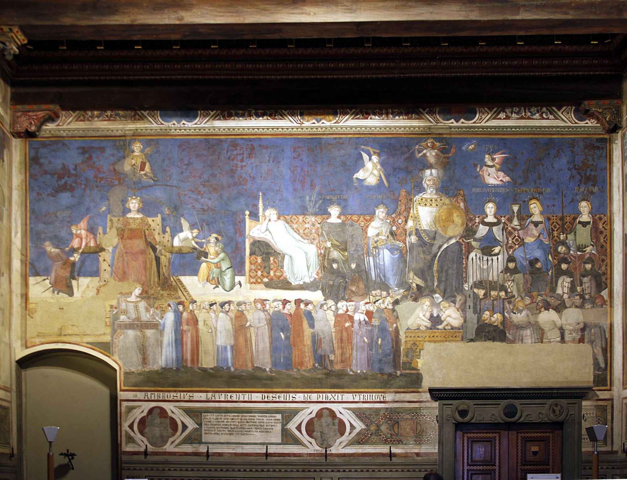 A wide view of Ambrogio Lorenzetti's grand medieval fresco cycle lining the walls of the Palazzo Pubblico, showing the comprehensive vision of civic justice and its real-world effects.