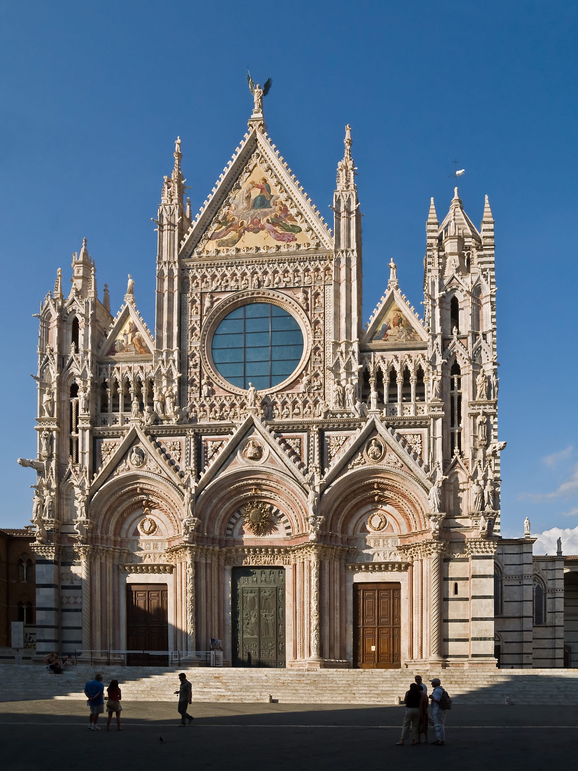 The Gothic facade of the Siena Cathedral in polychrome marble, featuring sculptures by Giovanni Pisano and a large central rose window.