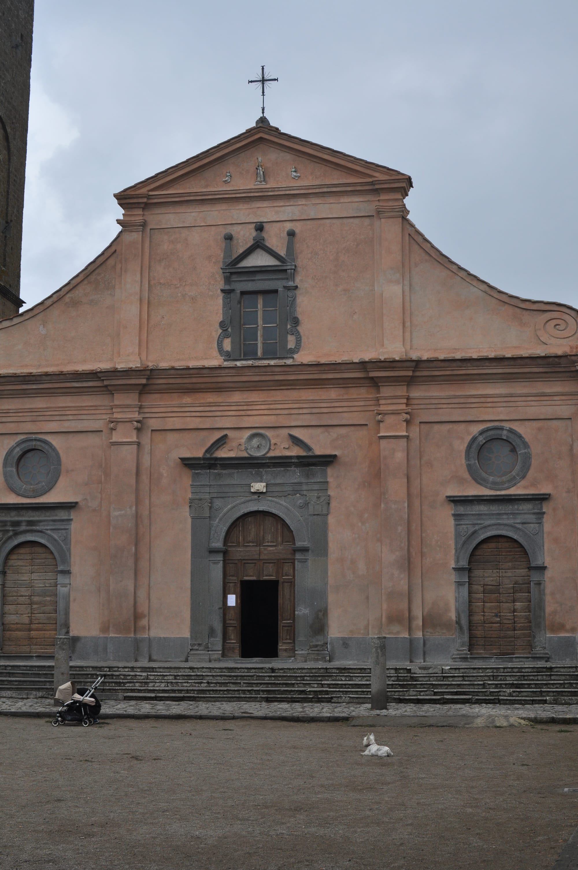 Front view of the Renaissance facade of San Donato Church in a deserted dirt square, featuring a single white dog lying peacefully on the ground.