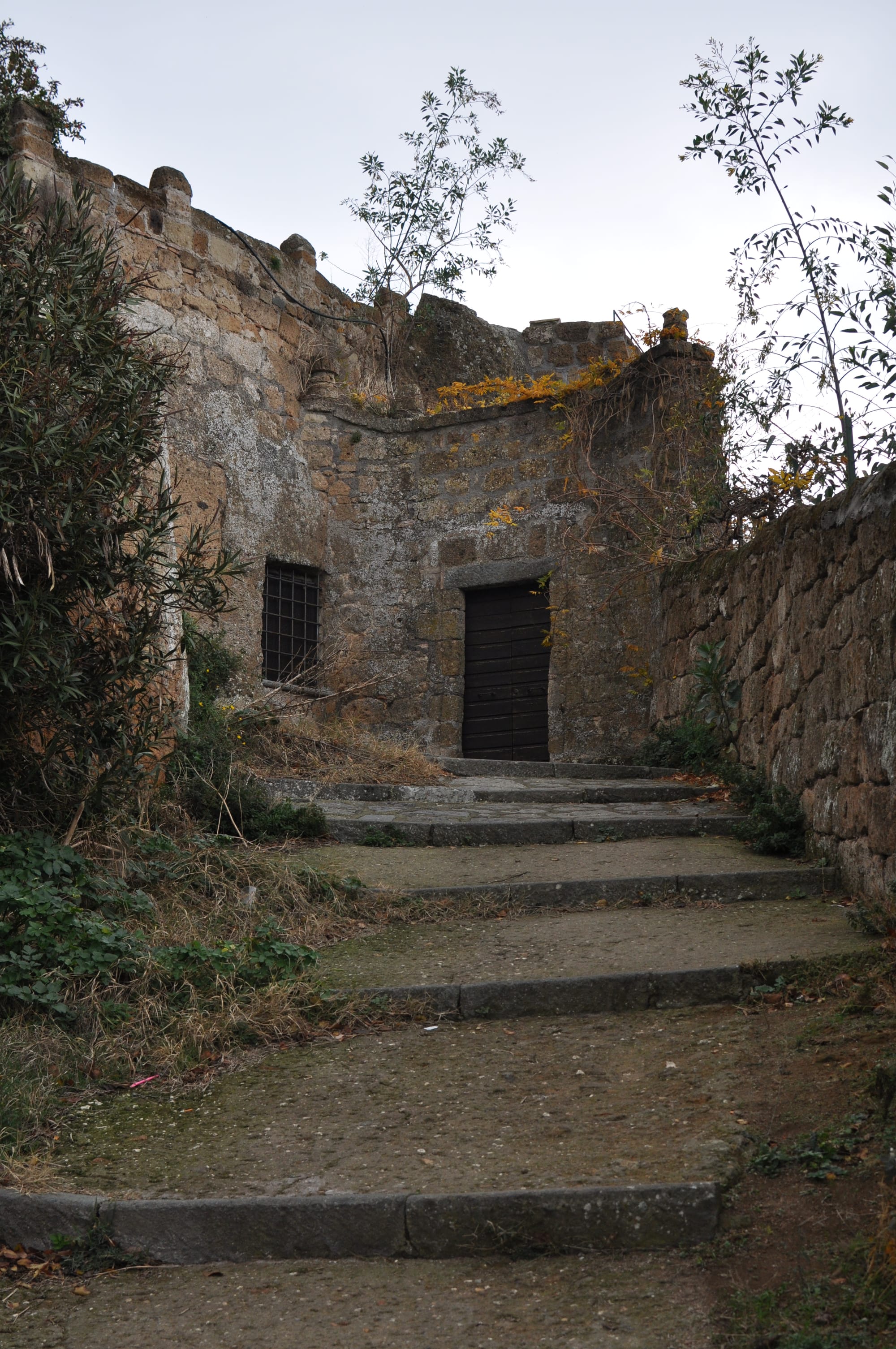 A curved stone path with wide steps leads up toward a dark, closed wooden door built into an ancient tufa stone wall.