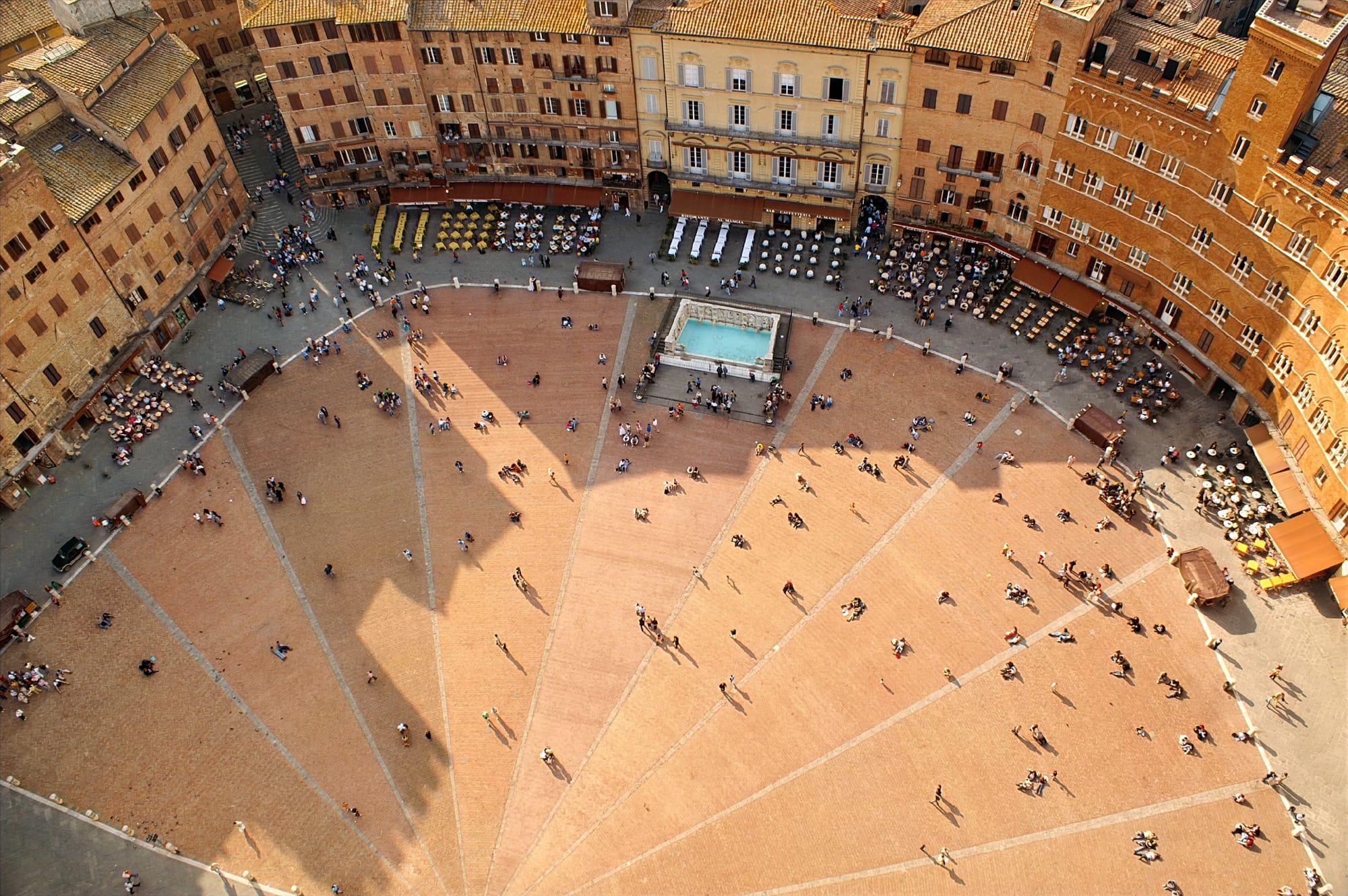 Looking down at Piazza del Campo in Siena, showing the red brick pavement divided into nine distinct sections by white travertine strips.