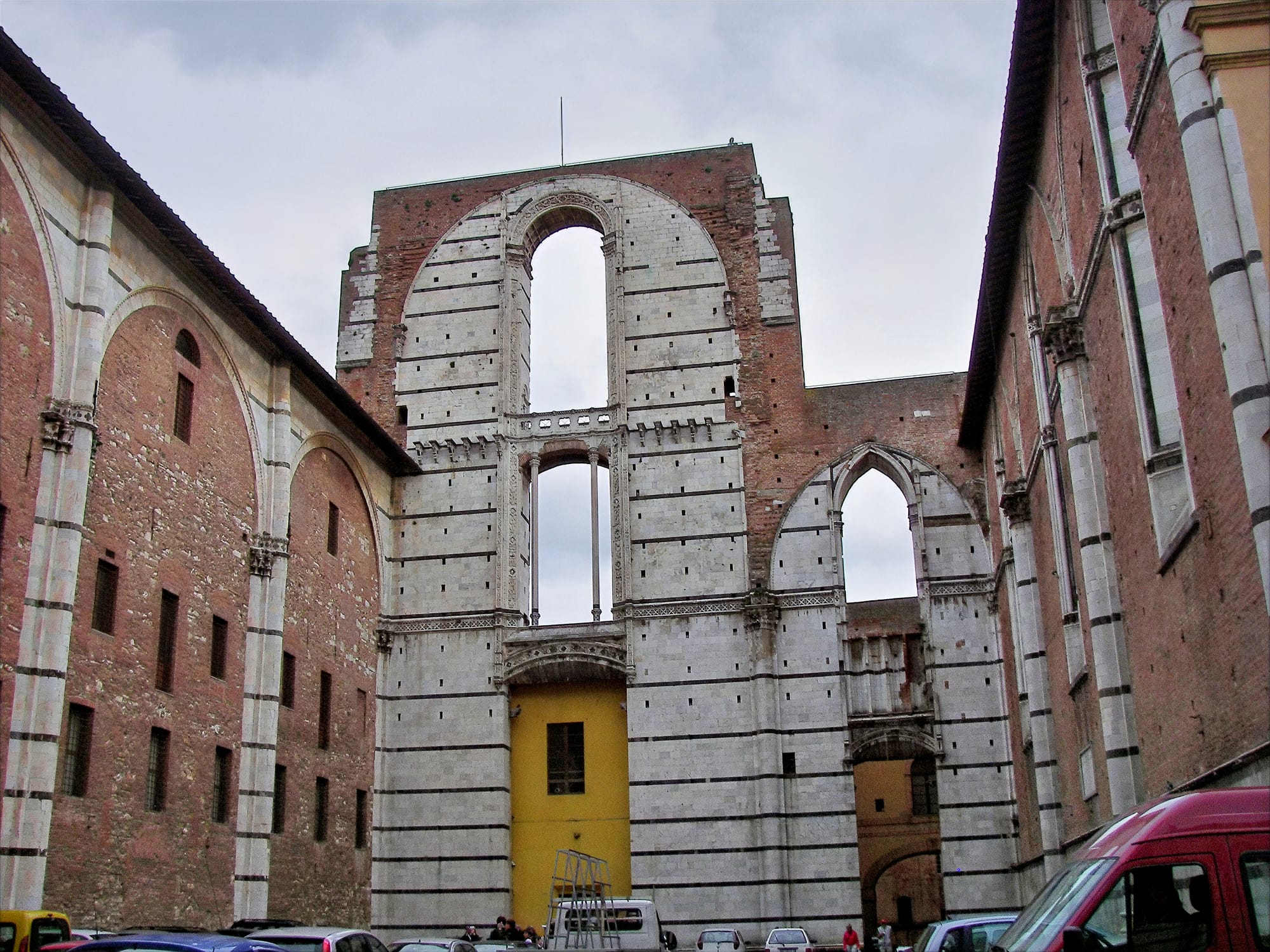 The ruins of the Duomo Nuovo in Siena, featuring high Gothic arches in stone and brick left unfinished and open to the sky.