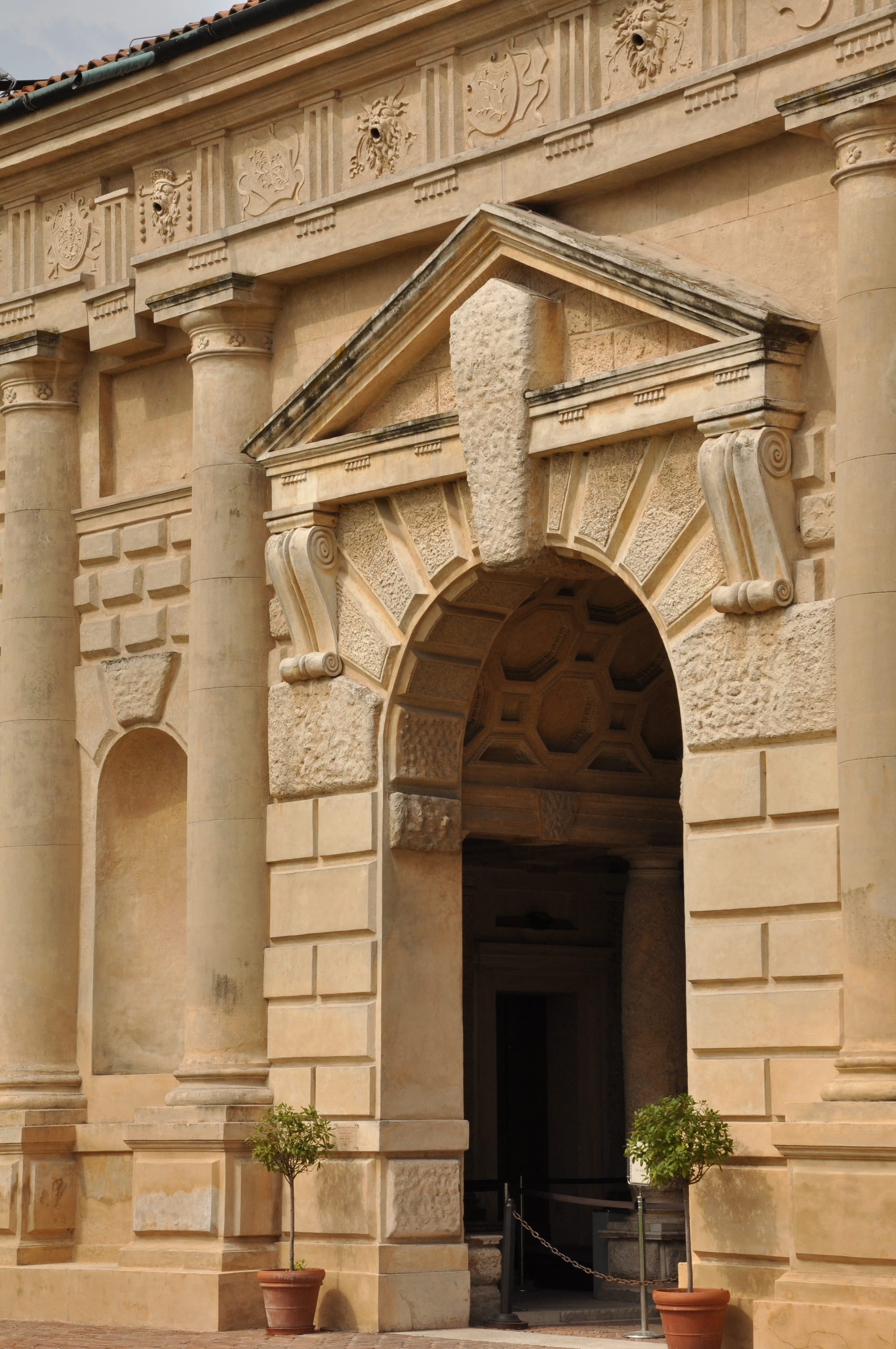 Close shot of an arched entrance with a prominent keystone breaking the pediment, showing a glimpse of the inner coffered ceiling.